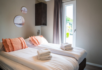Dormitorio moderno con dos camas individuales, cojines naranjas y toallas frescas en Wood Lodge Waterzicht.