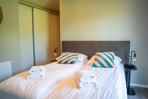 Dormitorio en Wood Lodge Waterzicht con dos camas, cojines de colores y toallas limpias ordenadamente dobladas.
