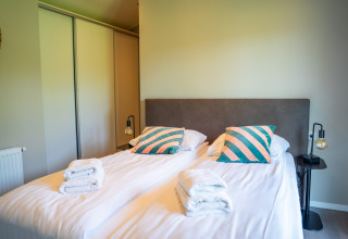 Camera da letto presso Wood Lodge Waterzicht con due letti singoli, cuscini colorati e asciugamani freschi.