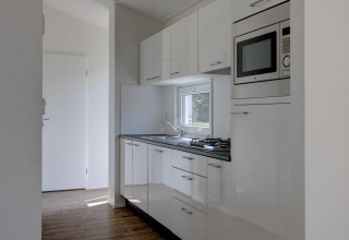 Cocina pequeña moderna en Wood Lodge del Holiday park Molenvelden, Países Bajos, con gabinetes blancos.