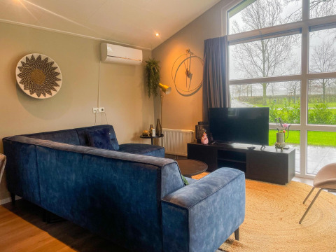 Moderne stue i Wood Lodge på Holiday park Molenvelden med store vinduer og blå sofa, Holland.