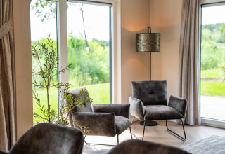 Cozy lounge with two gray armchairs, tall lamp, and large windows overlooking a lush green garden.
