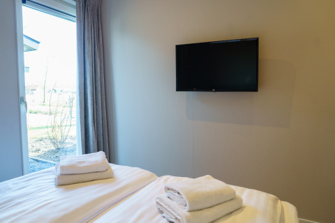 Moderne soveværelse på Villa Veldzicht i Holiday park Molenvelden med seng, tv og vindue ud til have.
