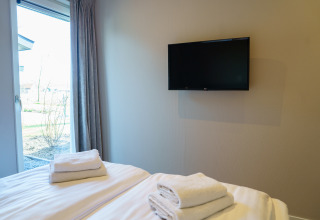 Dormitorio moderno en Villa Veldzicht, Holiday park Molenvelden, con cama, TV y ventana al exterior.