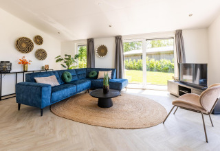 Moderne stue med blå hjørnesofa, rattan-tæppe og store vinduer på Villa Waterzicht Luxe med Hottub 4.