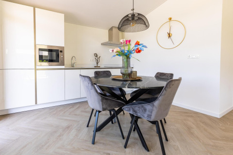 Cuisine et coin repas modernes à la Villa Waterzicht Luxe avec table noire, chaises grises, et horloge murale.