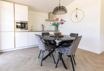 Moderne keuken en eetruimte in Villa Waterzicht Luxe met ronde zwarte tafel, grijze stoelen en klok.