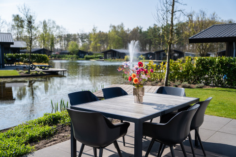 Table extérieure avec vase fleuri, vue sur le lac et fontaine à la Villa Waterzicht Luxe met Hottub 6, Molenvelden.