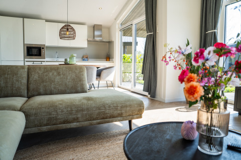 Moderne lodge med elegant stue, køkken, stor sofa, blomster og store vinduer med udsigt, Villa Waterzicht Luxe.