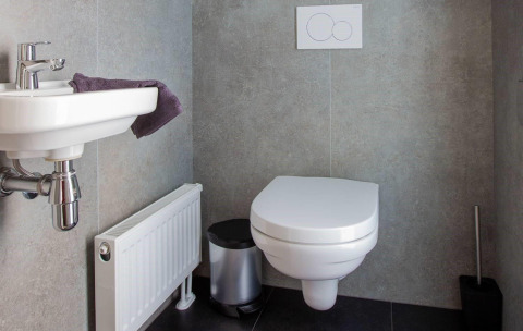 Baño moderno con inodoro suspendido, pequeño lavabo, toalla, radiador y papelera en una elegante cabaña.