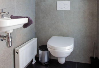 Bagno moderno con wc sospeso, piccolo lavabo, asciugamano, termosifone e cestino in una lodge elegante.