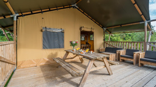 Overdekt terras bij een Glampinglodge safaritent met houten meubels, bloemen en een ontbijttafel.