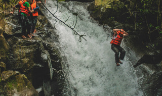 Menschen mit Schwimmwesten springen einen Wasserfall in einem tropischen Park herunter, voller Abenteuer.