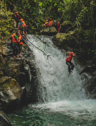 Des personnes en gilets de sauvetage sautent d'une cascade dans la jungle, profitant d'activités d'aventure.