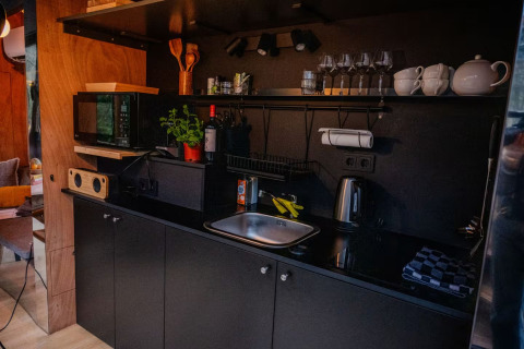 Pequeña cocina moderna con armarios negros y utensilios en Slowlodge Echo, Zomerlicht, Países Bajos.