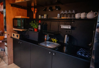 Modern kitchenette with black cabinets, herb plant, microwave and wine glasses at Slowlodge Echo, Netherlands.