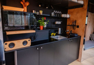 Moderne sort tekøkken med mikroovn, håndvask og urter, set indendørs på Slowlodge Echo i Zomerlicht.