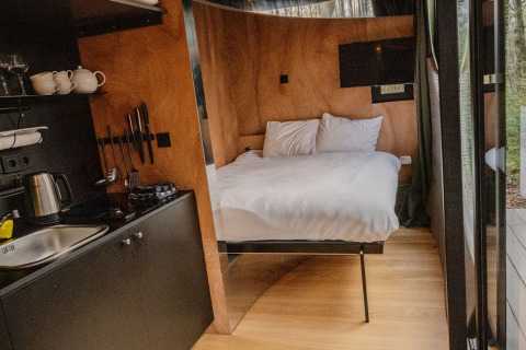 Indvendig udsigt til Slowlodge Echo ved Zomerlicht i Nederlandene med seng, tekøkken og træinteriør.