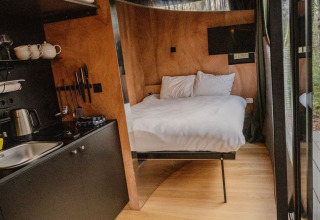 Indvendig udsigt til Slowlodge Echo ved Zomerlicht i Nederlandene med seng, tekøkken og træinteriør.