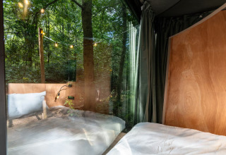 Udsigt fra et soveværelse i Slowlodge Echo ved Zomerlicht, Nederlandene, med træer og lyskæder udenfor.