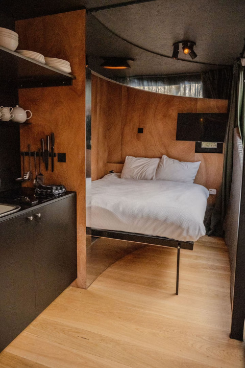 Moderne lodge med træinteriør, komfortabel seng og kompakt køkken i Slowlodge Echo, Zomerlicht, Holland.