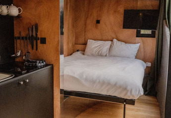 Moderne lodge med træinteriør, komfortabel seng og kompakt køkken i Slowlodge Echo, Zomerlicht, Holland.