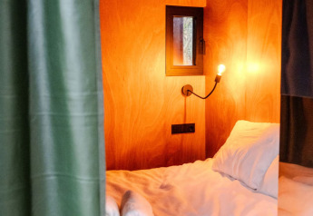 Letto in cabina di legno con asciugamani arrotolati, luce calda e finestra al Slowlodge Echo, Zomerlicht.