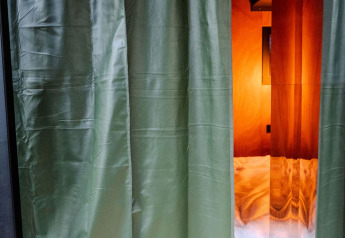 Tende verdi parzialmente aperte che svelano camera moderna illuminata presso Slowlodge Echo a Zomerlicht, Olanda.
