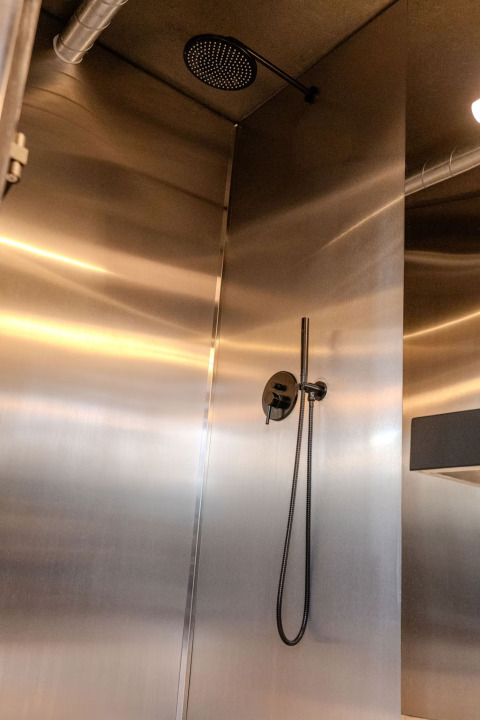 Stainless steel shower with modern black fixtures at Slowlodge Echo, Zomerlicht, Netherlands, industrial style.