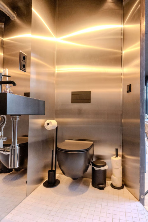 Moderne badeværelse med sort toilet og rustfrit stålvægge på Slowlodge Echo, Zomerlicht, Holland.