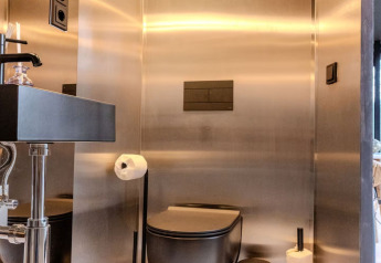 Moderne badeværelse med sort toilet og rustfrit stålvægge på Slowlodge Echo, Zomerlicht, Holland.