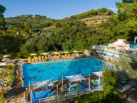 Udendørs swimmingpool med glade feriegæster, liggestole og parasoller, omgivet af grønne bakker i Toscana.