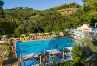 Udendørs swimmingpool med glade feriegæster, liggestole og parasoller, omgivet af grønne bakker i Toscana.
