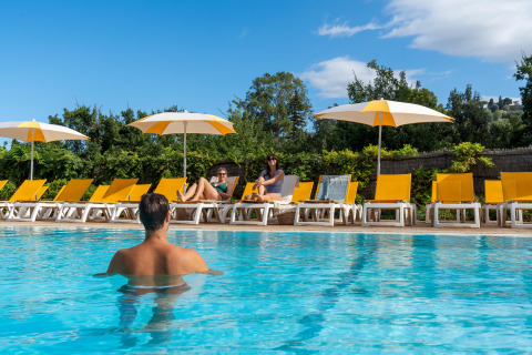 Personer slapper af ved poolen med gule liggestole og parasoller på Sandaya Le Pianacce i Toscana, Italien.