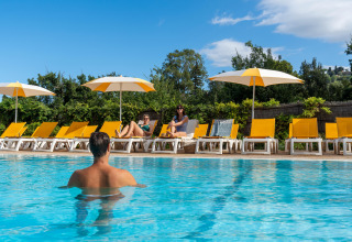 Personer slapper af ved poolen med gule liggestole og parasoller på Sandaya Le Pianacce i Toscana, Italien.