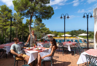 Gæster nyder udendørs spisning med udsigt til pool og pinjetræer på Sandaya Le Pianacce i Toscana.