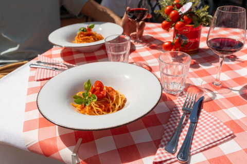 To pastaretter med tomatsauce og et glas rødvin på et bord med rødternet dug i Toscana, Italien.