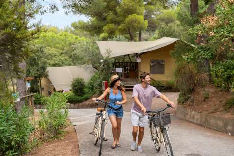 Et par går med cykler foran en lodgetelt i naturen på Sandaya Le Pianacce, en feriepark i Toscana, Italien.