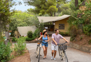 Et par går med cykler foran en lodgetelt i naturen på Sandaya Le Pianacce, en feriepark i Toscana, Italien.