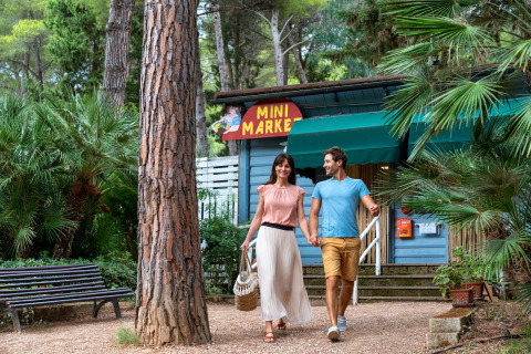 Et ungt par går hånd i hånd foran en mini-marked i Sandaya Le Pianacce feriepark i Toscana, Italien.