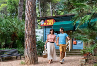 Et ungt par går hånd i hånd foran en mini-marked i Sandaya Le Pianacce feriepark i Toscana, Italien.