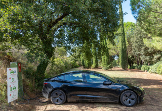 En sort elbil lader op ved en ladestation omgivet af træer i Sandaya Le Pianacce, Toscana, Italien.