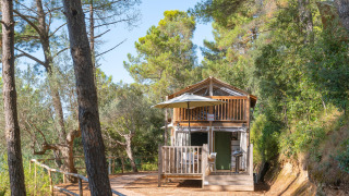 Twee verdiepingen tellende safaritent Lodge Bamboo, omringd door groen, veranda en een parasol buiten.