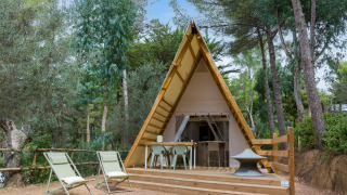 Luxe A-frame lodge in het bos met terras, tafel, stoelen en twee ligstoelen aan de voorkant.