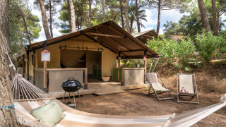 Safari tent Kenya in het bos, met hangmat, barbecue en loungestoelen bij het houten terras voor het tent.