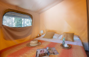 Vista interna di una tenda safari con letto matrimoniale, cuscini e finestra al Tent Kenya, Sandaya Le Pianacce, Italia.