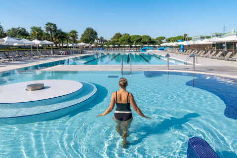 Woman enters swimming pool at Sandaya Europa Village holiday park in Veneto, Italy, surrounded by loungers.