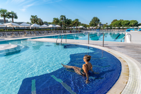 Woman relaxing in a pool at Sandaya Europa Village holiday park in Veneto, Italy, with umbrellas in the background.