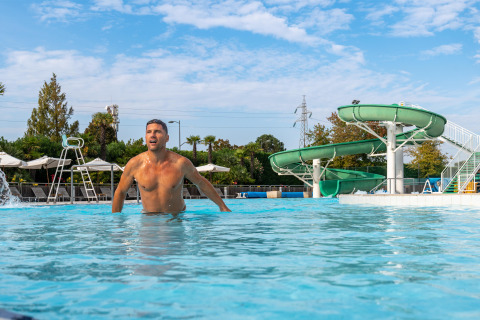 Hombre en la piscina del Sandaya Europa Village en Véneto, Italia, con tobogán verde de fondo al aire libre.