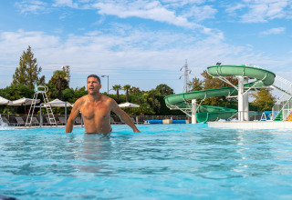 Uomo nella piscina al Sandaya Europa Village in Veneto, Italia, con uno scivolo verde sullo sfondo.